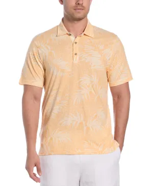 A man is wearing a light orange polo shirt with a subtle palm leaf pattern, paired with white pants.