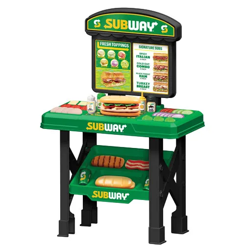 Toy Subway sandwich shop playset with a green countertop, fake food items like subs and toppings, and a menu board displaying sandwich options.