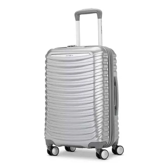 Silver Samsonite carry-on spinner featuring a textured, ribbed design with four multidirectional wheels, a telescopic handle, and a side handle for easy transport.