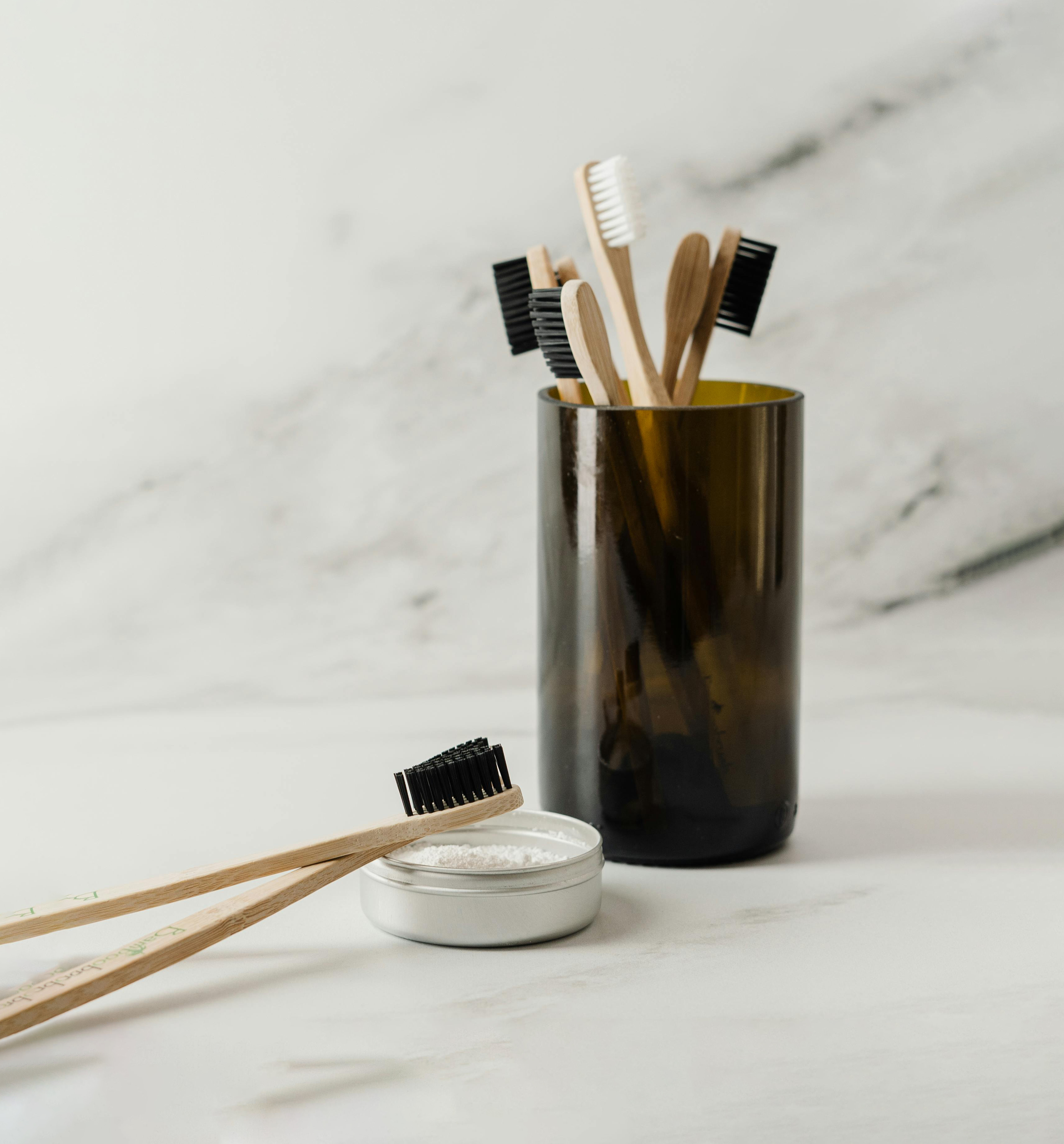 Bamboo toothbrushes in a smoked glass holder and tooth powder in a small open container with a brush resting on top.