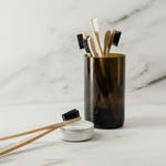 Bamboo toothbrushes in a smoked glass holder and tooth powder in a small open container with a brush resting on top.