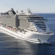 A large, modern cruise ship sails on the ocean, featuring multiple decks and numerous windows.