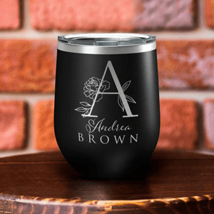 A black insulated wine tumbler features the letter \“A\“ adorned with a floral design and the name \“Andrea Brown\“ engraved below.