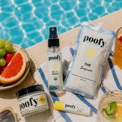 A poolside scene features Poofy Bath & Body products, including SPF 30 sunscreen, after sun spray, face and body cream, and lip balm, alongside a towel, grapefruit, grapes, and drinks.