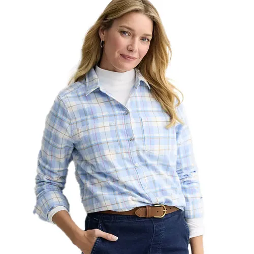 A woman is wearing a light blue plaid button-up shirt over a white turtleneck, paired with dark jeans and a brown belt.
