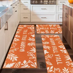 Three orange kitchen rugs with white leaf patterns and text reading \“HAPPY FALL Y'ALL\“ and \“HELLO FALL\“ placed on a wooden floor in a kitchen setting.