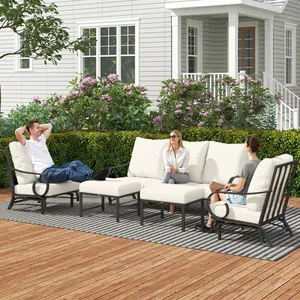 Outdoor patio seating set with metal frames and white cushions, featuring a loveseat, two armchairs, a coffee table, and an ottoman on a deck with floral and leafy surroundings.