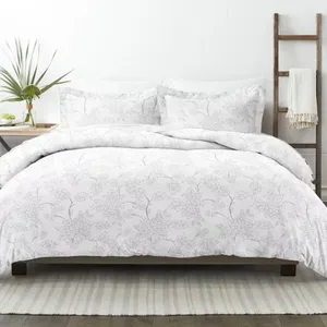 A white floral-patterned bedding set on a bed, accompanied by two matching pillowcases. The setting includes a side table with a vase and a ladder with a draped blanket.