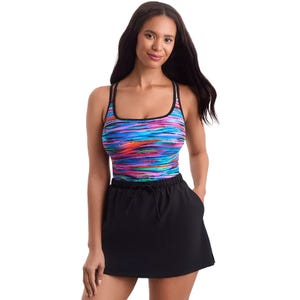 A woman is wearing a colorful, striped swimsuit top with thin straps and a square neckline, paired with a black skort with a drawstring waist.