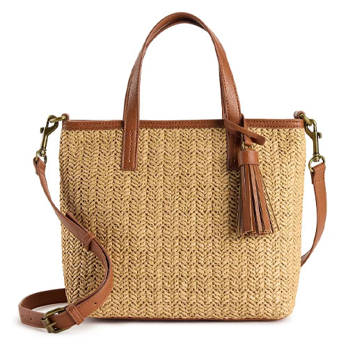 A straw tote bag with brown leather handles and a detachable crossbody strap, featuring a woven texture and a tassel accent.