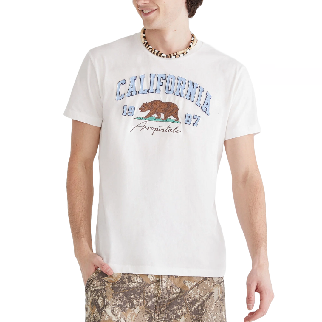 White T-shirt with \“California\“, \“1967\“, and Aeropostale printed on it, featuring a bear graphic. Paired with camouflage-patterned pants and a beaded necklace.