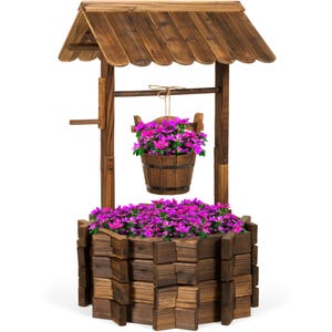 A decorative wooden wishing well planter with a roof, holding vibrant pink flowers in the hanging bucket and around the base.