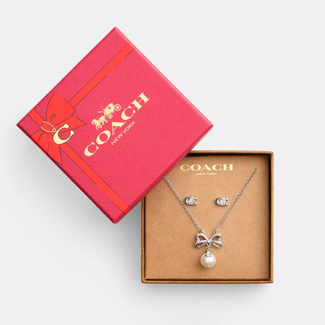 Coach Outlet CZ Necklace & Studs Set features a silver-tone chain with a bow and pearl pendant, accompanied by matching cubic zirconia stud earrings, presented in a red gift box with a gold Coach New York logo.