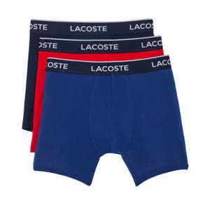 Three pairs of Lacoste boxer briefs in navy, red, and blue, each with a black waistband featuring the brand name in white.