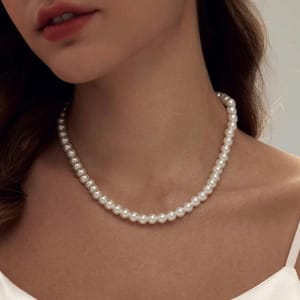 A woman wearing a simple, elegant pearl necklace with a strand of uniformly sized white pearls, paired with a white top.