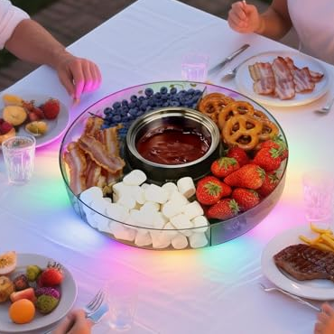 LED-illuminated fondue set on a table, featuring a chocolate dip surrounded by marshmallows, strawberries, pretzels, bacon, and other snacks, with people enjoying a meal.
