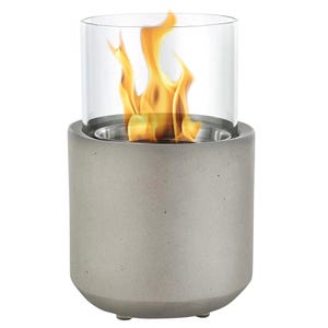 A tabletop fireplace with a cylindrical concrete base and a clear glass enclosure, showcasing visible flames.