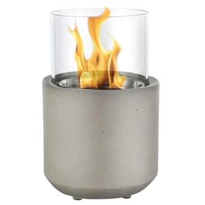 A tabletop fireplace with a cylindrical concrete base and a clear glass enclosure, showcasing visible flames.
