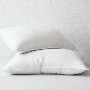 Two white cooling gel pillows with subtle stripes, stacked against a light-colored textured wall.