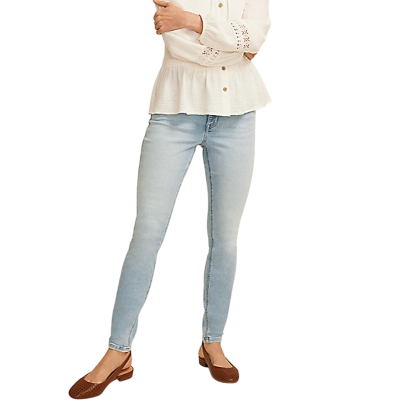 A person wears light blue skinny jeans paired with a white peplum blouse featuring eyelet details and brown slingback flats.