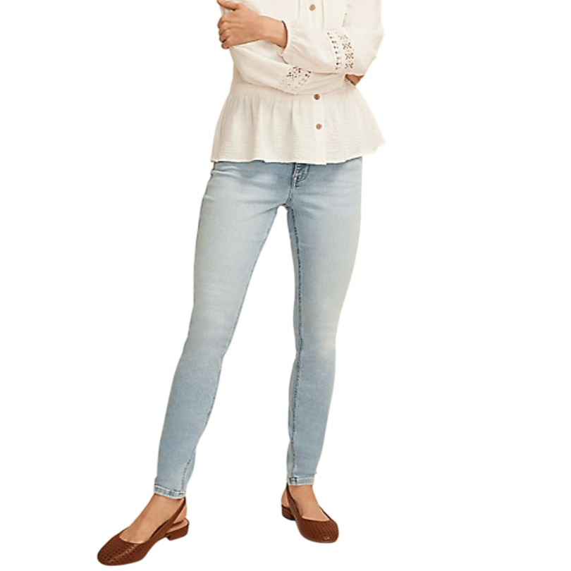 A person wears light blue skinny jeans paired with a white peplum blouse featuring eyelet details and brown slingback flats.