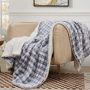 A cozy, textured fur throw blanket with a quilted design draped over a beige chair, set against a modern art piece and next to a checkered rug.