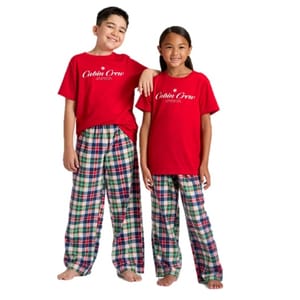Two children wearing matching plaid pajama pants and red t-shirts with \“Cabin Crew\“ printed on them.