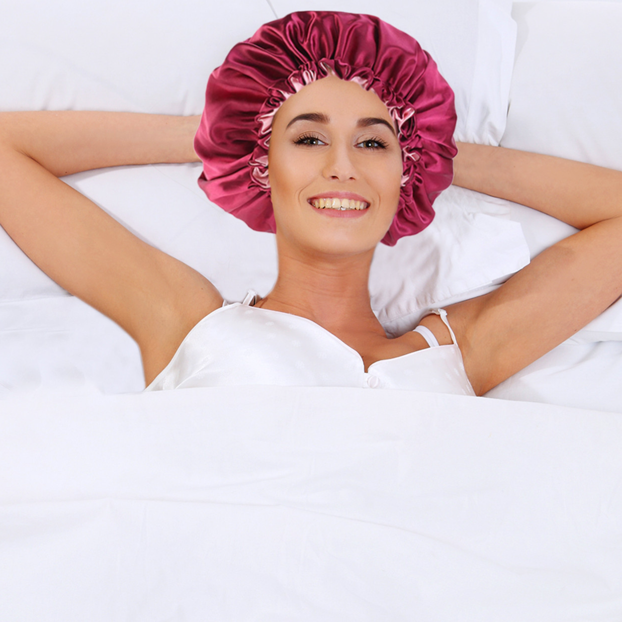 A person is lying in bed wearing a pink satin bonnet and a white satin nightgown. The setting suggests comfort and relaxation.