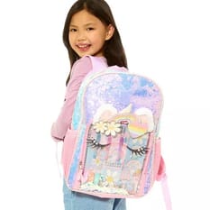 A girl is wearing a sparkling backpack with pastel colors, featuring decorative eyelashes, flowers, and a rainbow. The backpack has pink straps and appears to have a transparent section with additional decorations.