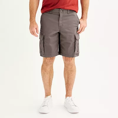 A man is wearing gray cargo shorts that reach above the knee, with multiple pockets on the sides, a button closure, and white sneakers.