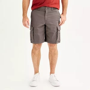 A man is wearing gray cargo shorts that reach above the knee, with multiple pockets on the sides, a button closure, and white sneakers.