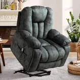 A plush, dark gray reclining lift chair with a side pocket contains a remote control, placed in a cozy living room setting with plants and a fireplace.