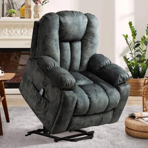 A plush, dark gray reclining lift chair with a side pocket contains a remote control, placed in a cozy living room setting with plants and a fireplace.