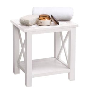 A white wooden bench with a slatted top and an X-frame design on the sides, featuring a lower shelf, a towel, and toiletry items on top.