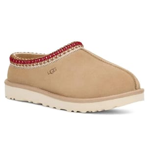 A tan-colored slip-on shoe with a thick white sole, featuring UGG branding and red stitching along the upper rim.