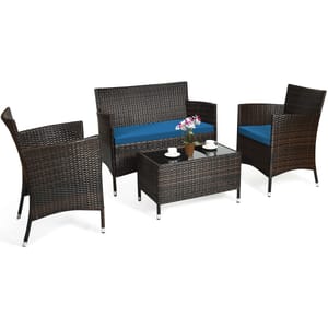 4-piece patio furniture set with a glass-top coffee table, two armchairs, and a loveseat, all with brown wicker frames and blue cushions. Includes three cups, saucers, and a potted plant on the table.