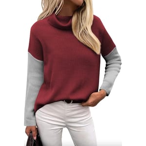 A stylish women's turtleneck sweater featuring a maroon body with contrasting gray sleeves. It has a relaxed fit and pairs well with white pants for a chic look.