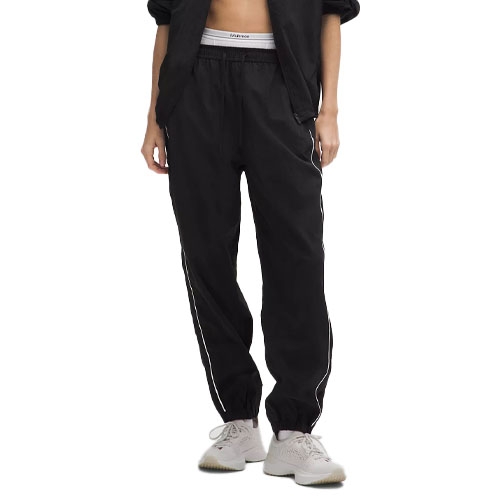 A person is wearing black athletic jogger pants with white stripes along the sides, paired with a white waistband and light-colored sneakers.