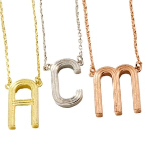 Three necklaces featuring gold, silver, and rose gold initial pendants: \“A\“ in gold, \“C\“ in silver, and \“M\“ in rose gold.