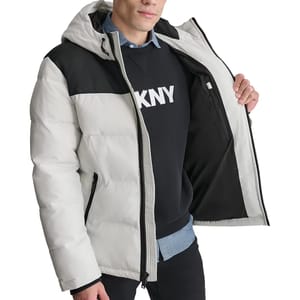 A man is wearing a color-blocked puffer jacket with a hood, showing the inner pocket, over a DKNY sweatshirt and a denim shirt.