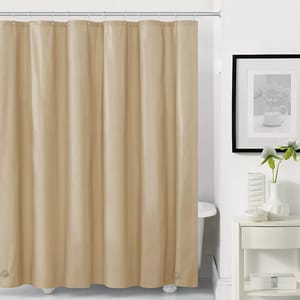 A plain beige shower curtain liner is shown, hanging from a shower rod, with a white shelf, a plant, and a framed picture in the background.