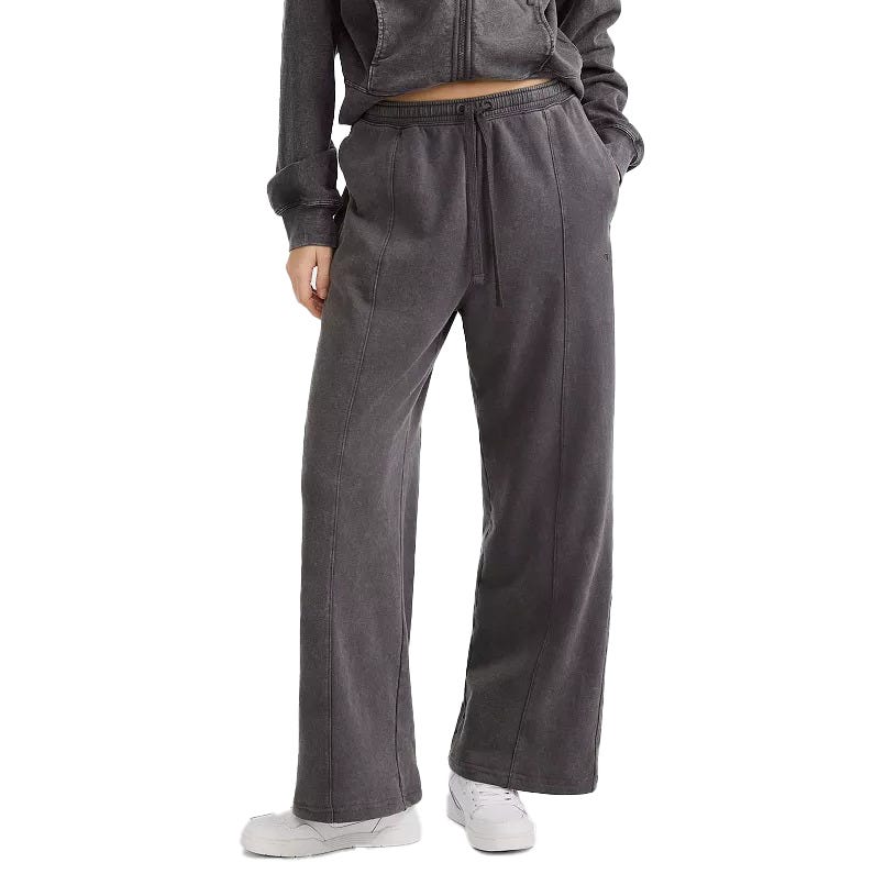 A person is wearing a dark gray drawstring sweatpants and matching zip-up hoodie, paired with white sneakers. The outfit has a comfortable, casual style with wide-leg pants and side pockets.