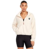 A woman is wearing a beige fleece quarter-zip pullover with a logo patch on the chest and black cycling shorts, standing against a white background.