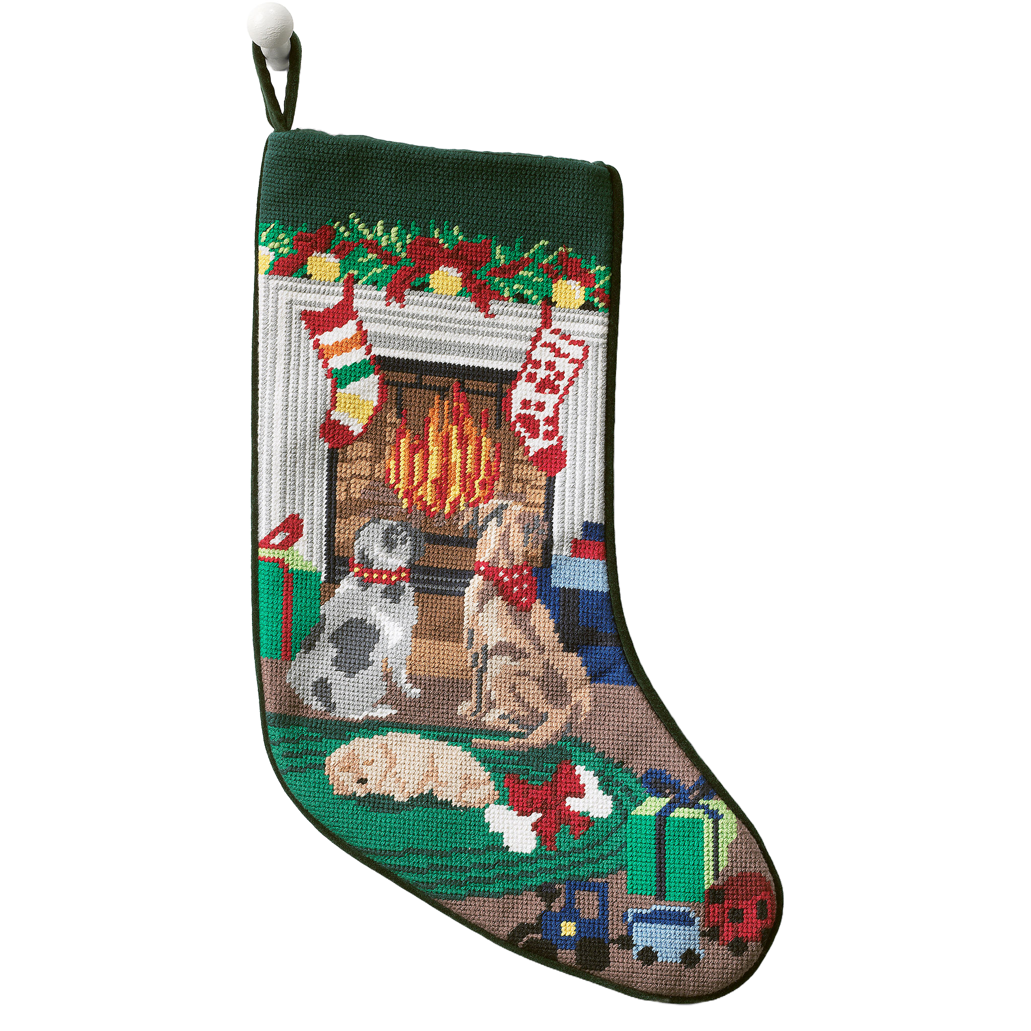 A festive needlepoint stocking featuring three dogs near a fireplace, adorned with holiday decorations. Two stockings hang above the fire, surrounded by wrapped gifts and toys. The design is colorful and detailed, capturing a cozy holiday scene.