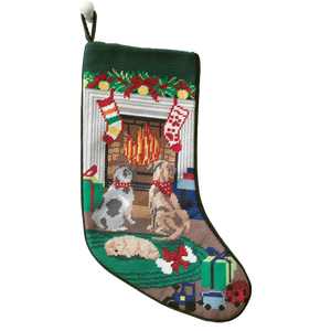 A festive needlepoint stocking featuring three dogs near a fireplace, adorned with holiday decorations. Two stockings hang above the fire, surrounded by wrapped gifts and toys. The design is colorful and detailed, capturing a cozy holiday scene.