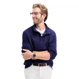 Man wearing a navy quilted pullover with white pants, a striped shirt underneath, glasses, and a watch.