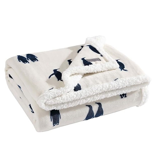 A cream-colored Eddie Bauer throw blanket with a Sherpa lining and a pattern of navy blue fish.