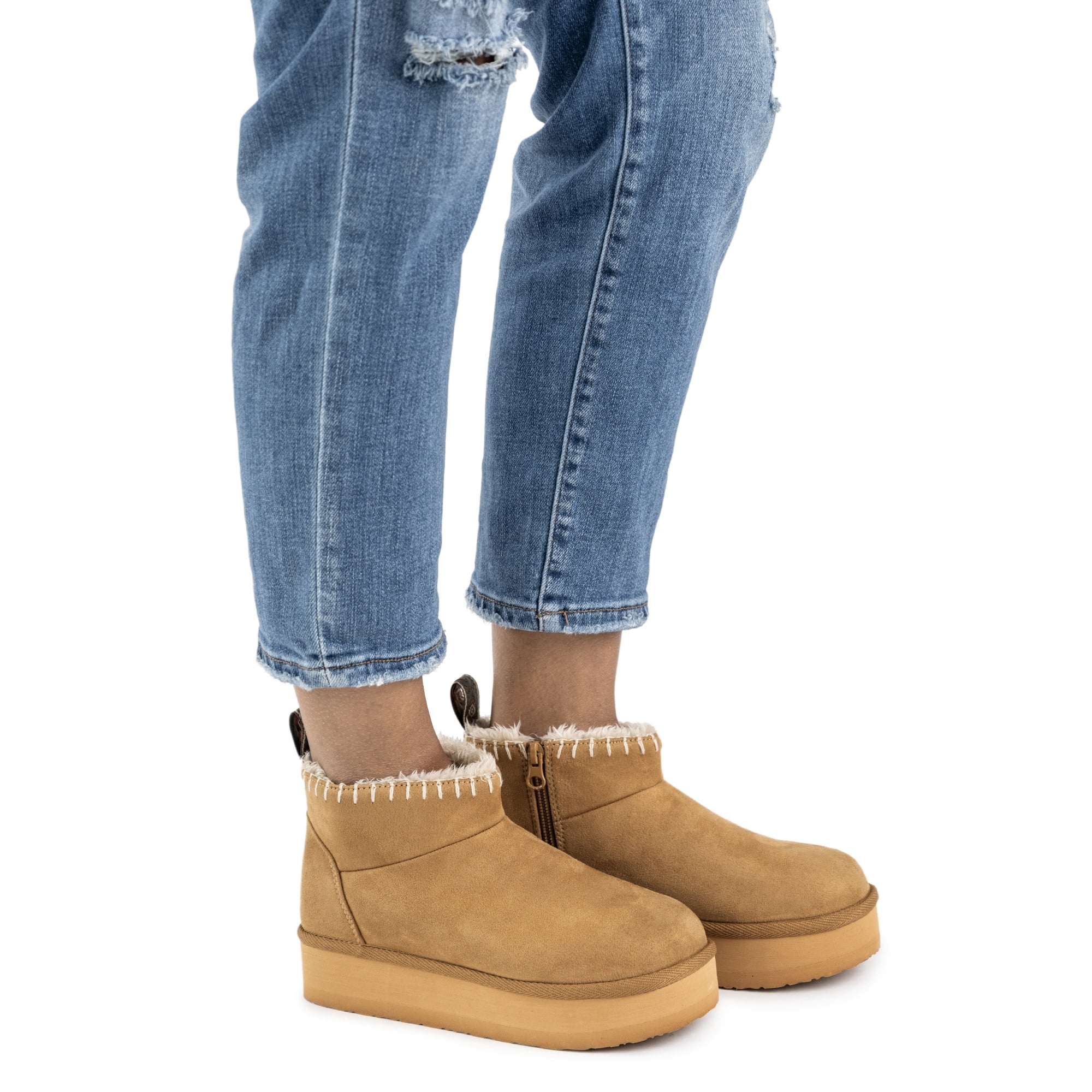Light brown suede Muk Luks boots with side zippers and a plush lining peeking out at the top, paired with ripped blue denim jeans.