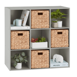 A gray cubical shelving unit holds three woven baskets, books, two small potted plants, a white elephant statue, and a rectangular planter with succulents.