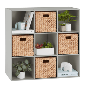 A gray cubical shelving unit holds three woven baskets, books, two small potted plants, a white elephant statue, and a rectangular planter with succulents.